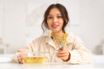 Young Asian woman preparing steam inhalation with herbs at table in bedroom