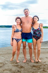 handsome elderly man standing on the beach with two women in bathing suits