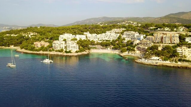 Retreating drone shot of the beachfront of Playa Illetas, off the coast of Mallorca in Palma Island, in Spain.