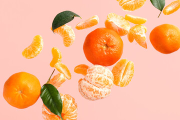 Flying sweet ripe mandarins and leaves on pink background