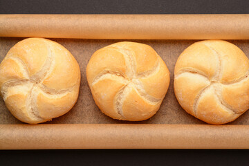 Baking paper with delicious kaiser rolls on black background