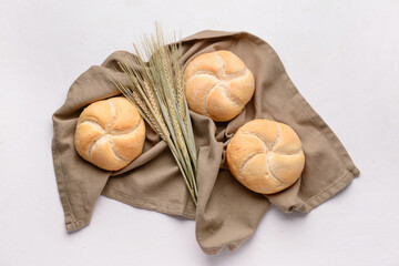 Napkin with delicious kaiser rolls and wheat ears on white background