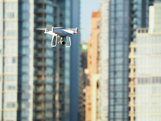 A white quadcopter drone flies outside a city.