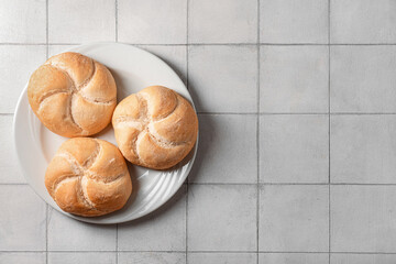 Plate with delicious kaiser rolls on grey tiled background