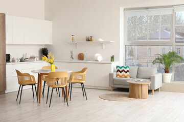 Interior of light spacious kitchen studio with dining table, mimosa flowers, armchairs, houseplant,...