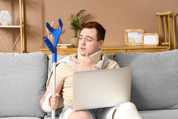 Injured young man after accident with crutch and laptop video chatting on sofa at home