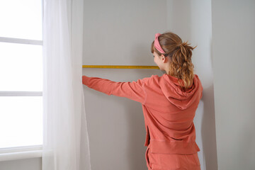 Fototapeta na wymiar Young woman measuring wall during repair in bedroom
