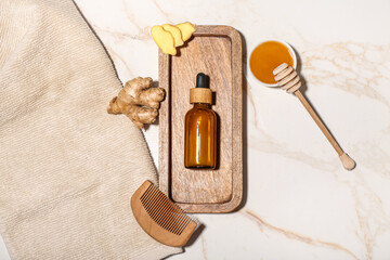 Composition with bottle of essential oil, ginger, honey and hair comb on light background
