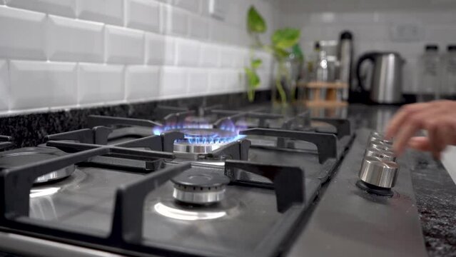 Mano de mujer encendiendo hornalla grande doble corona de estufa a gas natural en contexto de cocina moderna