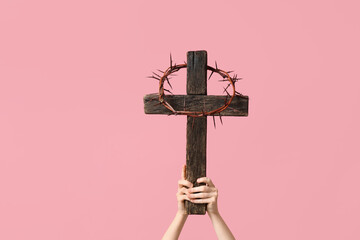 Female hands with with wooden cross and crown of thorns on pink background. Good Friday concept