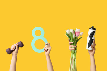 Female hands with paper figure 8, sports equipment and tulips for International Women's Day on yellow background - obrazy, fototapety, plakaty