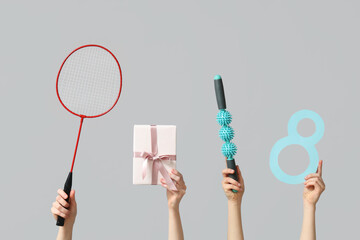 Female hands with paper figure 8, sports equipment and gift box for International Women's Day on grey background