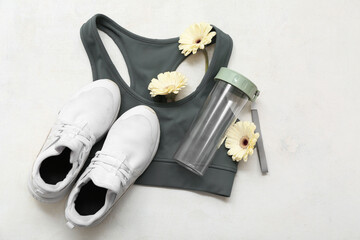 Composition with sports bra, shoes, bottle of water and flowers on light background. International...