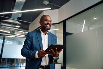 Happy mature black man in businesswear with digital tablet in corridor of office
