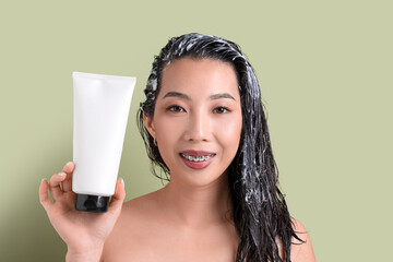 Young Asian woman with tube of hair mask on green background, closeup