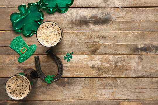 Glasses of dark beer with plastic eyeglasses, horseshoe and decor for St. Patrick's Day celebration on wooden background