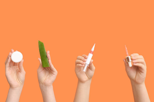 Female hands holding cuticle oil pen with pipette, aloe vera and jar of cream on orange background
