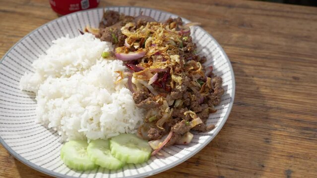 Full plate of beef larb with white rice and sliced cucumbers, slider 4K