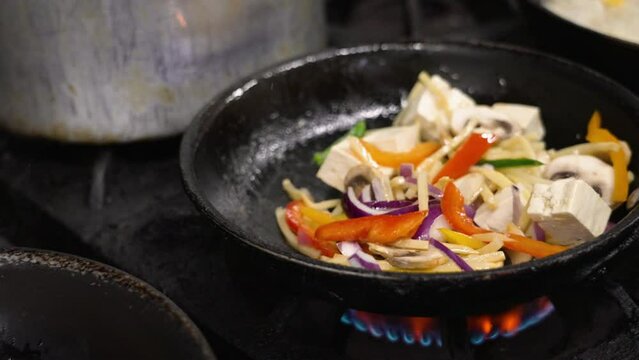 Stirfrying vegetables and tofu over high heat in commercial kitchen, tossing cooking vegetable, slow motion close up 4K