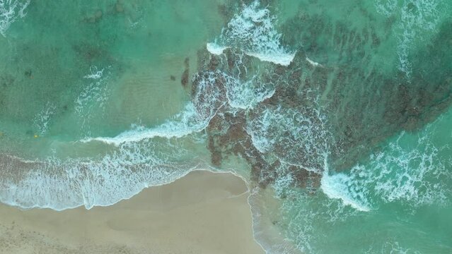 Aerial top down shot of waves reaching beach in Cyprus. Coral and rocks underwater. 