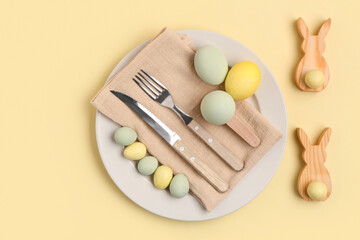 Beautiful table setting with Easter eggs and wooden bunnies on yellow background