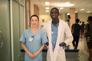 Asian and American doctor Successful team of medical doctors are looking at camera and smiling while standing in hospital.