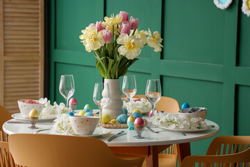Stylish Easter table setting, painted eggs, glasses and vase of flowers in dining room