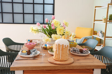 Stylish festive table setting, painted eggs, Easter cake and vase of flowers in dining room