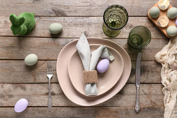 Table setting for Easter celebration with green bunny toy and painted eggs on wooden background....