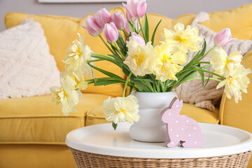 Vase with beautiful tulips and toy bunny on table in living room decorated for Easter celebration