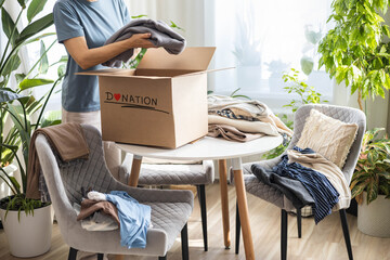 Donation concept. A woman collects clothes at home in a box for donation, recycling or disposal.