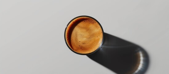 A black and brown cortado coffee cup is placed on a table with a gray background, casting strong shadows. The cup is the focal point of the composition, showcasing its sleek design and color contrast.