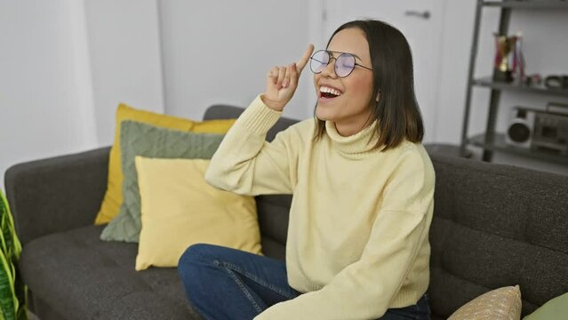 Young beautiful hispanic woman wearing glasses pointing finger up with successful idea. exited and happy. number one. at home
