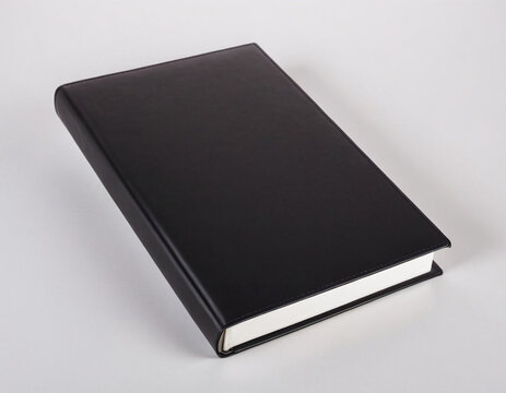 A closed black hardcover book lies on a plain white surface, symbolizing mystery and potential within its pages.
