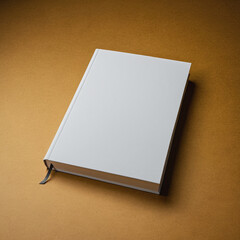 Hardcover book with a blank white cover placed on a warm, golden surface in soft lighting.