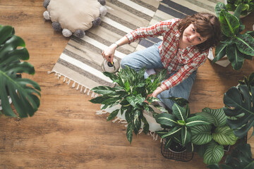 A young woman enjoys caring for flowers. Watering indoor plants and admiring them. 