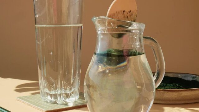 Add Natural organic green spirulina algae powder to water drink on neutral beige background. Chlorella seaweed vegan superfood cocktails smoothie supplement source and detox drinking. Innovative