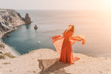 Woman red dress sea. Female dancer in a long red dress posing on a beach with rocks on sunny day. Girl on the nature on blue sky background.