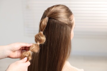 Naklejka premium Professional stylist braiding woman's hair indoors, closeup