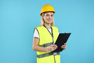 Engineer in hard hat holding clipboard on light blue background