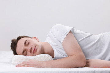 Fototapeta na wymiar Man sleeping on orthopedic pillow against light grey background