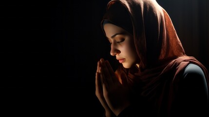 Obraz premium A beautiful young Muslim woman, wearing a traditional dress and hijab, Performs Divine services, Prays on a black background in a Mosque. Religion, Faith in God, Islam, Ramadan, Eid al-Adha concepts.