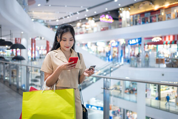 young woman in smart casual wear carrying many paper shopping bags shopping online on mobile phone...
