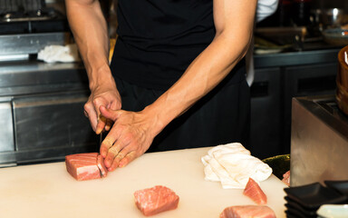 Sushi Chef Slices fresh tuna fish on the sushi bar. Chef cutting tuna fillet at professional...