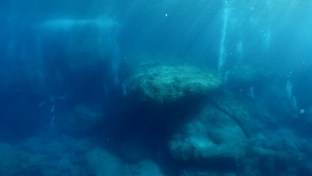 scuba divers exploring around a reef underwater deep blue water big rocks and bubbles ocean scenery 
