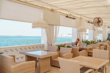 Woman coffee cafe laptop sea. Female freelancer using laptop on coffee break in modern cafe with sea view in the morning