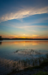 Fototapeta na wymiar Serene sunset over Graham Lake, in Maine, USA. Colorful sky reflected on rippled waters. Aquatic vegetation on the shoreline.