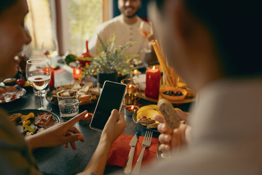 Close up of man and woman sitting at holiday dinner table at home and looking on mobile phone