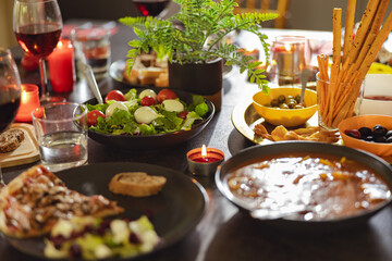 Cozy holiday table with different delicious food, beverages and candles ready for friends home party