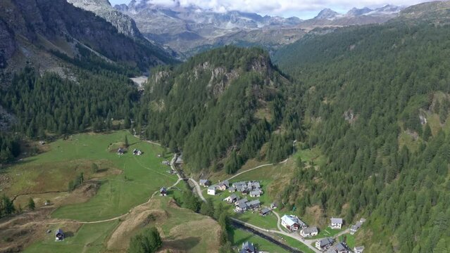 Lago di devero, alpe devero with rustic houses, green fields, and surrounding forests in daylight, aerial view